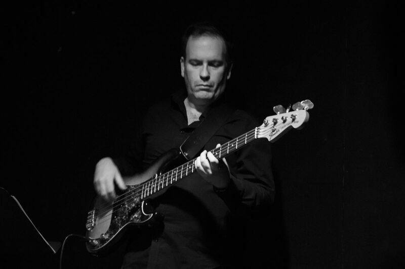 Rob Hutchinson playing electric bass on a dark stage
