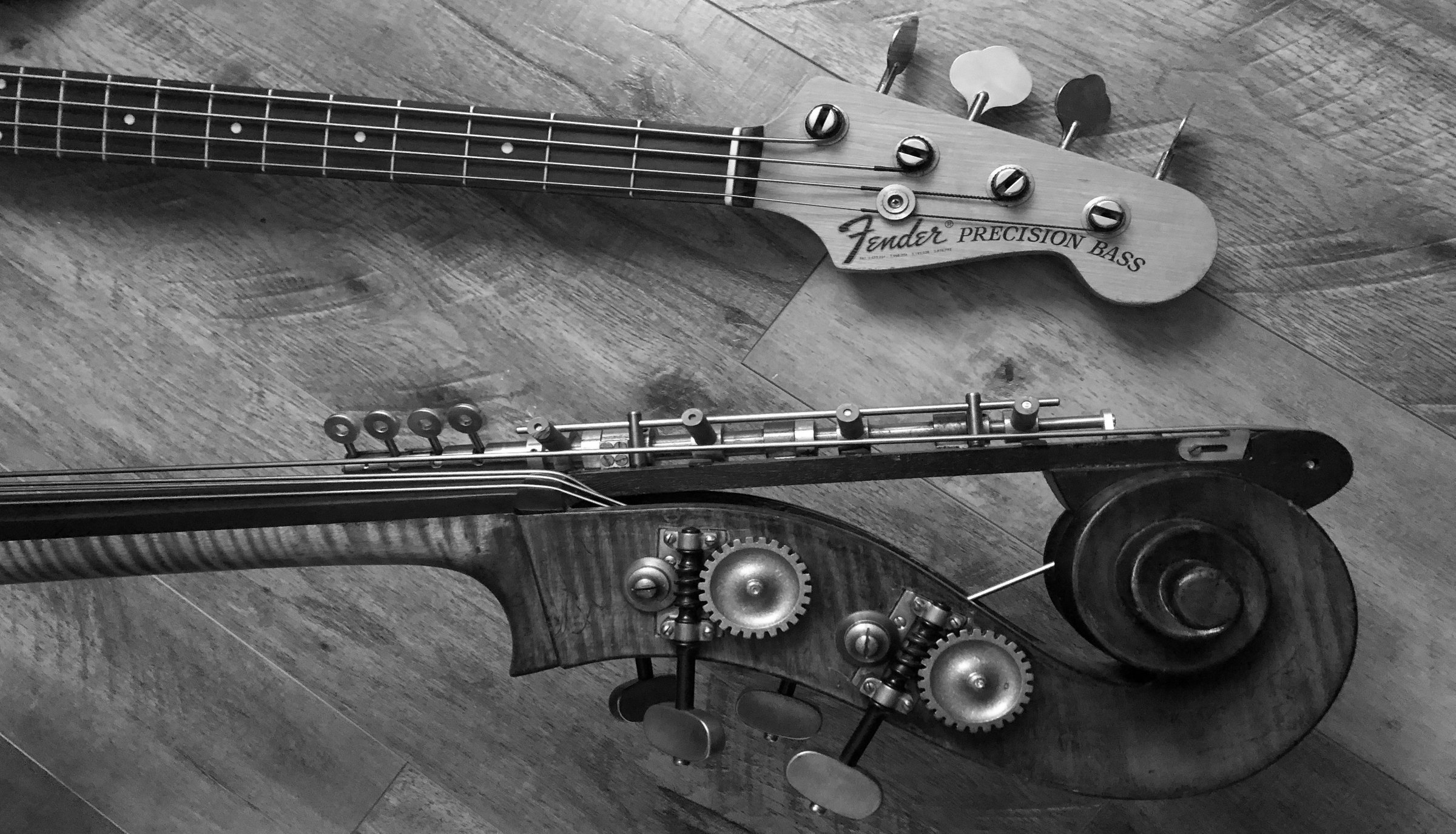 A Fender Precision Bass and a double bass scroll lying on a wooden floor